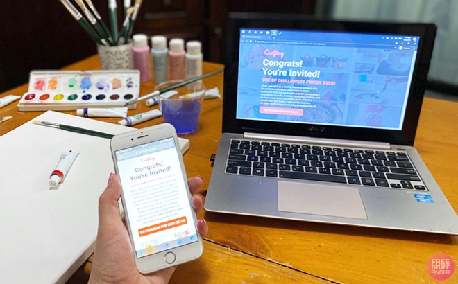 A Person Holding a Phone Displaying the Craftsy Offer With a Laptop and a Painting Kit in the Background