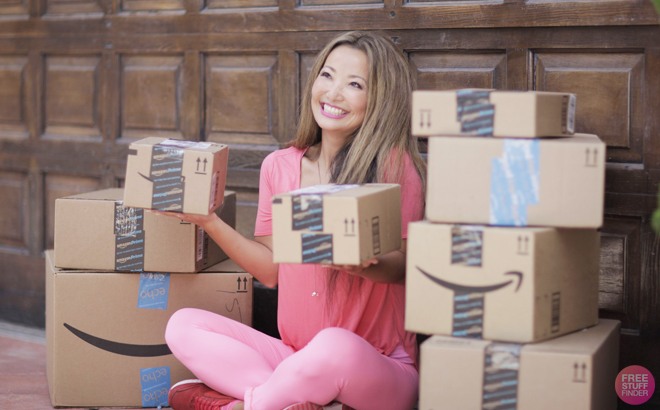 woman holding amazon boxes in both hands in front of a door with amazon boxes stacked around
