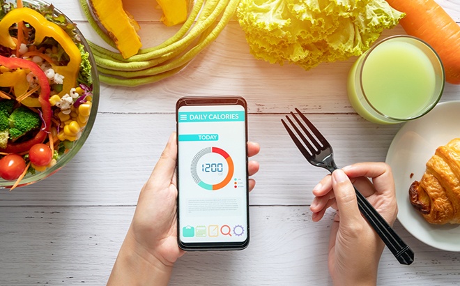 A Person Holding a Phone with Noom App on It While Eating Fresh Foods with a Fork