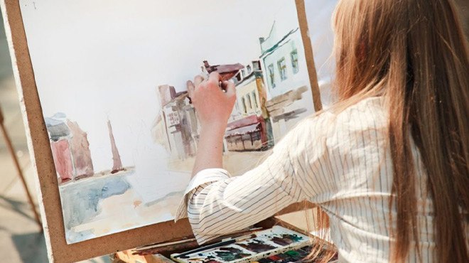 A Woman Painting a Picture of a Street With Houses