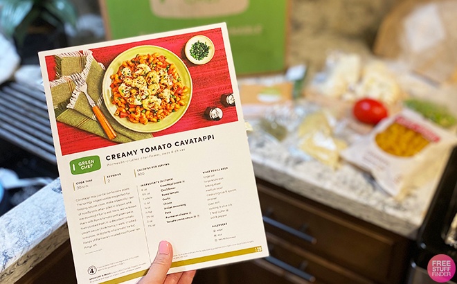 Hand Holding a Creamy Tomato Cavatappi Recipe with Ingredients in the Background