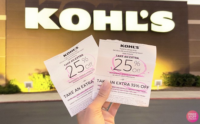 Hand Holding Kohl's Coupons for 25% off In Front of Kohl's Store Sign