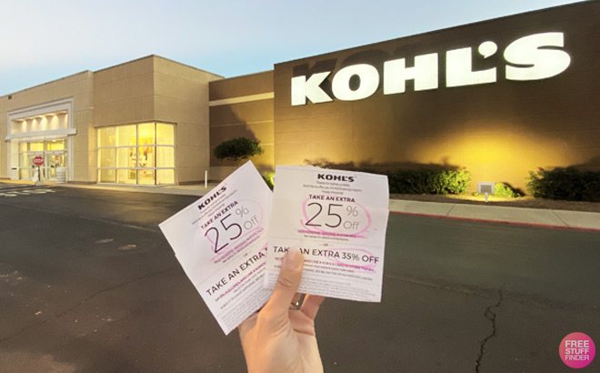 Hand Holding Two Kohl's Coupons for 25% off In Front of Kohl's Store Sign