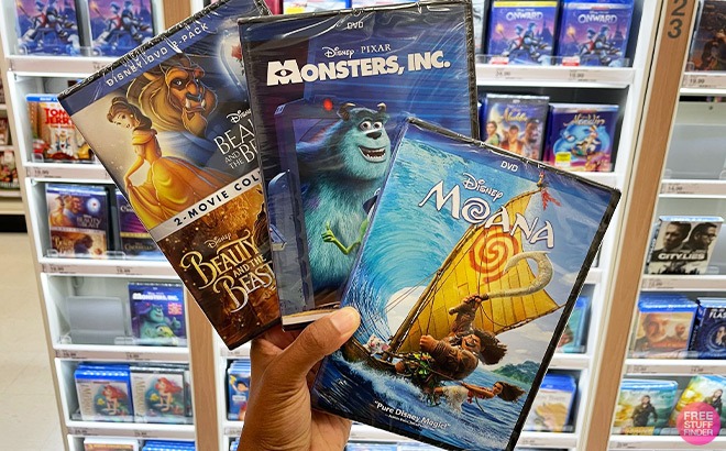 Hand Holding Disney Beauty and the Beast, Monsters INC and Moana Movie in Front of a Store Aisle
