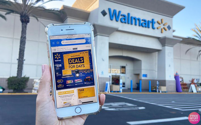 Hand Holding iPhone with Walmart Deals for Days Ad in Front of Walmart Store