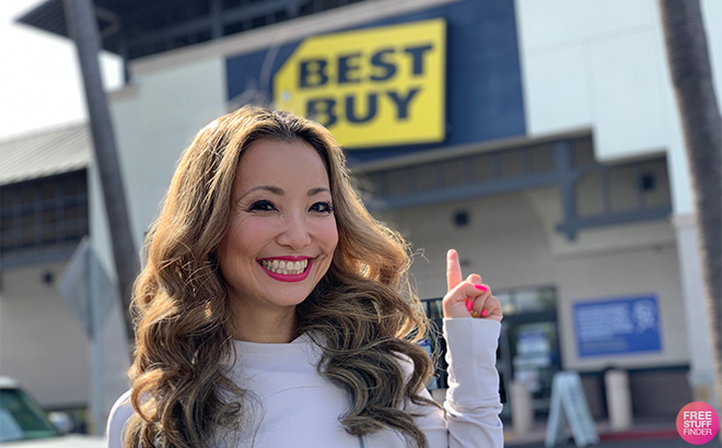 A Woman Standing in Front of a Best Buy Store Smiling and Pointing at the Store Sign