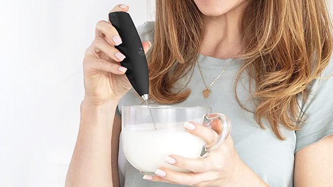 A Person Holding a Cup with Milk and Using a Handheld Milk Frother