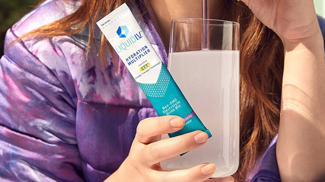 Woman Holding Liquid I.V. Hydration Multiplier in Concord Grape Flavor and a Glass
