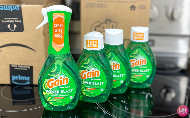 Gain Powerblast Dish Spray and 3 Refill Bottles on a Kitchen Stove with Amazon Boxes in the Background