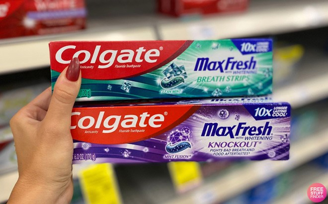 Hand holding two 6 Ounce Colgate Max Toothpastes