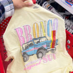A Hand Holding Ford Bronco Womens Oversized Graphic Shirt in Yellow Color at Target