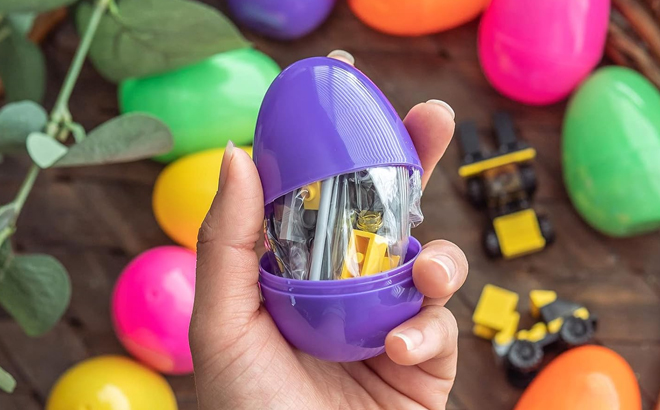 A Person Holding a Prefilled Easter Egg with Construction Vehicle with Many Other Same Eggs in the Background