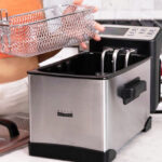 A Woman Holding Bella Pro Series Digital Deep Fryer Placed on a Marble Countertop