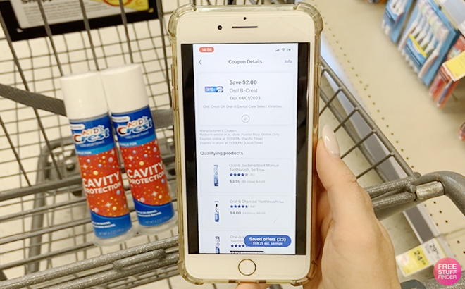 Hand Holding a Phone Showing Crest Oral B Digital Walgreens Coupon in Front of a Cart with Crest Kids Cavity Protection Toothpastes