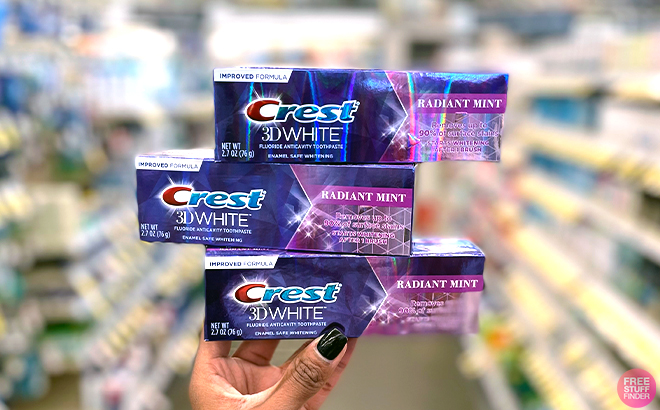 Hand holding three Crest 3D White Toothpastes