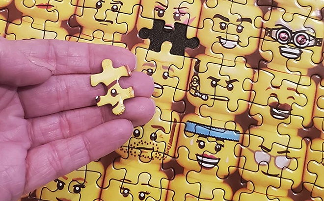 LEGO Minifigure Faces 1000 Piece Jigsaw Puzzle with a Piece in Hand
