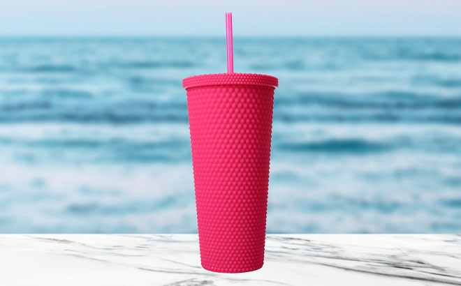 Magenta Reusable Diamond Tumbler 24 Ounce on a Marble Table and with an Ocean Background