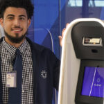 Man Standing Next to Clear Airport Security Pod