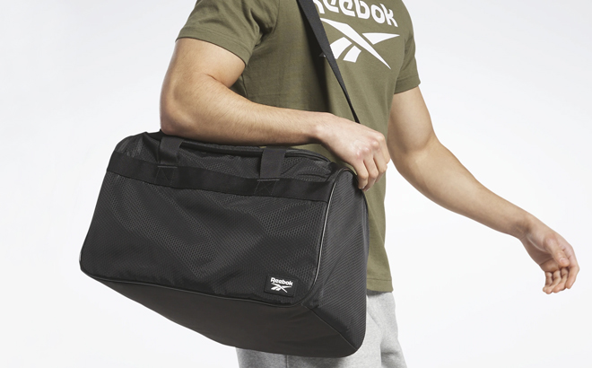 A Man Carrying Reebok Warrior II Duffel Bag Small in Black Color A Man Carrying Reebok Warrior II Duffel Bag Small in Black Color