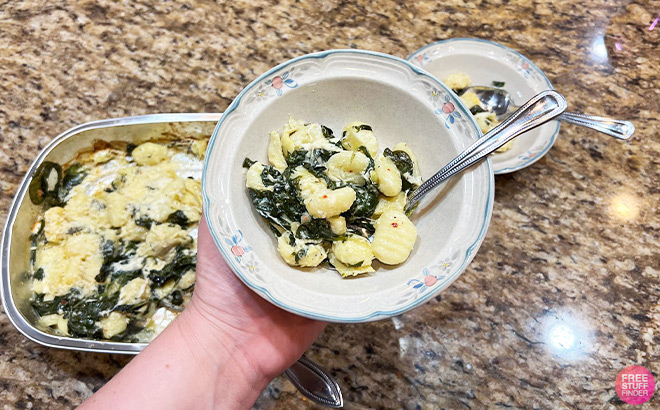 Hand Holding a Bowl of Gnocchi with Spinach on top of a Kitchen Countertop