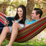 Two People Sitting on a Double Hammock Reading a Book