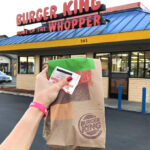 A Hand Holding Burger King Paper Bag in Front of Burger King Restaurant
