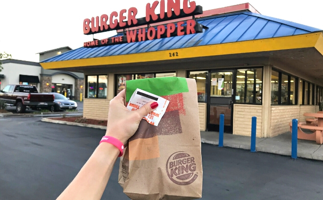 A Hand Holding Burger King Paper Bag in Front of Burger King Restaurant