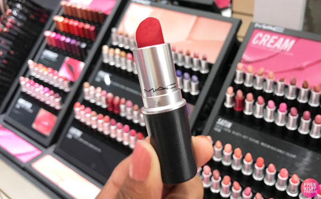 A Hand Holding a MAC Lipstick in Red Color with Background Showing Various MAC Lipsticks