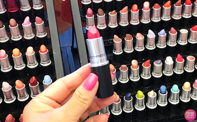 A Hand Holding a MAC Lipstick with Background Showing Various MAC Lipsticks
