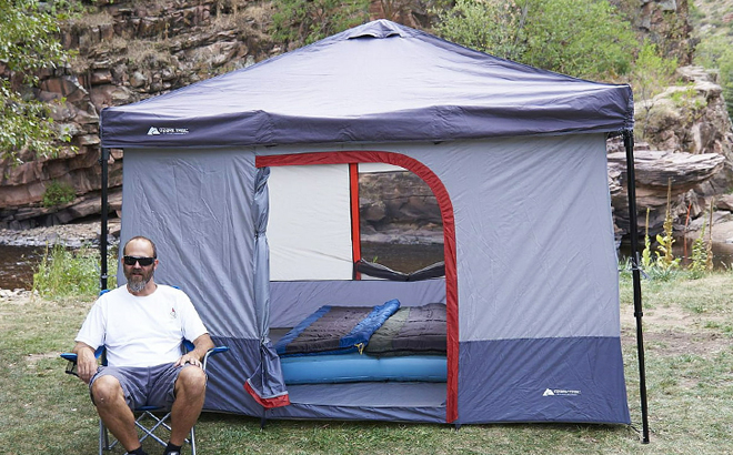 A Man Sitting on a Folding Chair Beside Ozark Trail ConnecTent 6 Person Canopy Tent
