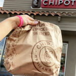 Hand Holding Chipotle Paper Bag in Front of Chipotle Store