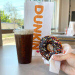 Hand Holding a Donut Next to a Dunkin Donuts Coffee and Bag