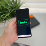 Hand Holding a Phone with the Word Hulu On The Background