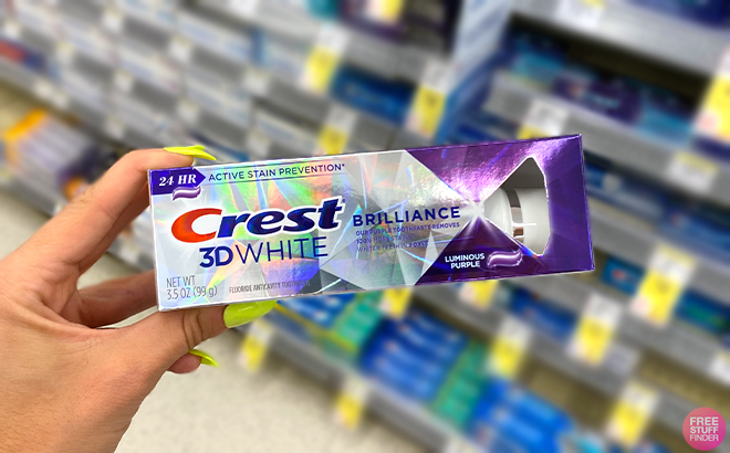 Hand holding one Crest 3D White Brilliance Toothpaste 3 5 Ounce