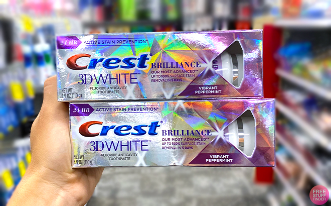 Hand holding two Crest 3D White Brilliance Toothpaste 3 9 Ounce
