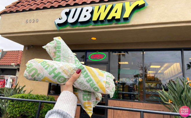 Person Holding 2 Subway Sandwiches in front of a Subway Store