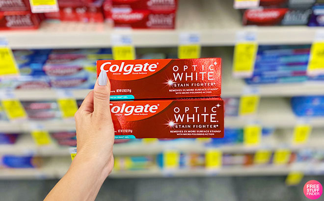 A Hand Holding 2 Colgate Optic White Toothpaste