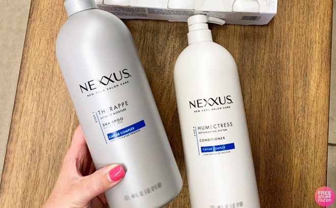 A Hand Holding Nexxus Shampoo and Nexxus Conditioner on a Table