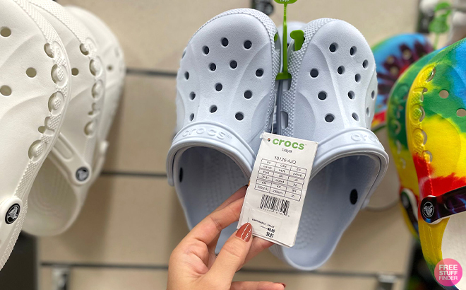 A Hand Holding the Tag of a Pair of Crocs Baya Clogs at a Store