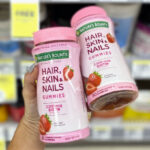 Hand holding two Natures Bounty Hair Skin and Nails Gummies with Biotin