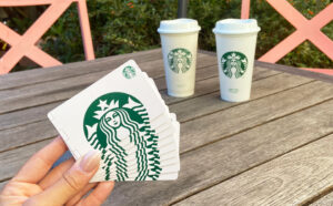 hand holding starbucks gift cards with starbucks cups in the back