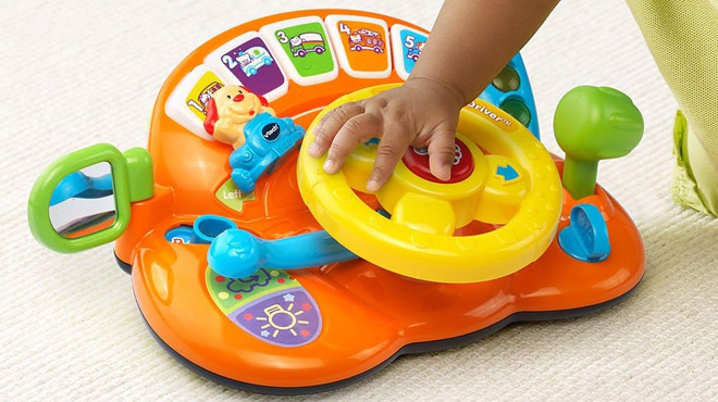 A Babys Hand with VTech Turn and Learn Driver Steering Wheel Toy in Orange Color