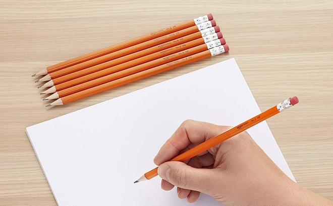 A Hand Holding Amazon Basics Pencils with a Paper and Six Pencils on the Table