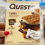 A Hand Holding a Box of Quest Protein Bars on a Shelf