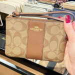 A Hand Holding Coach Oulet Corner Zip Wristlet In Signature Canvas