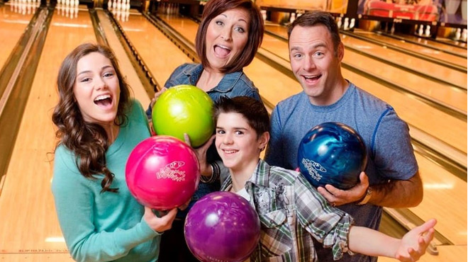 An entire Family of Four Holding Bowling Ball infront of the Bowling Alley