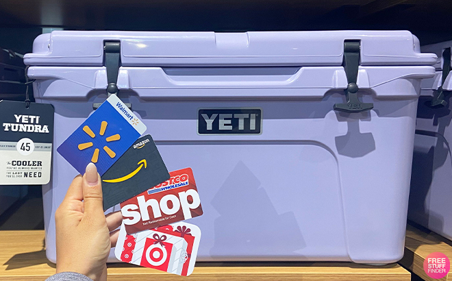Hand Holding Multiple Gift Cards in front of a YETI Tundra 45 Hard Cooler in Purple