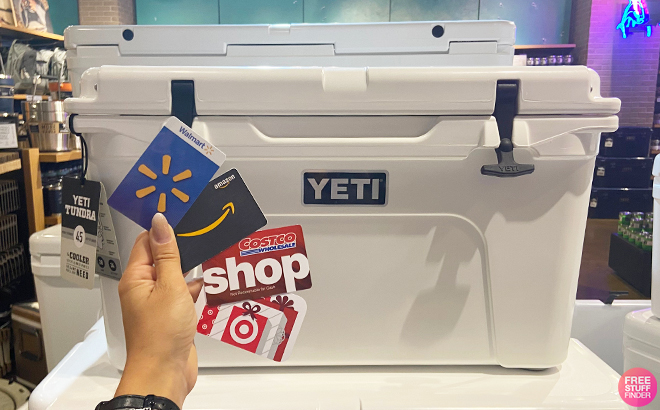 Hand Holding Multiple Gift Cards in front of a YETI Tundra 45 Hard Cooler in White