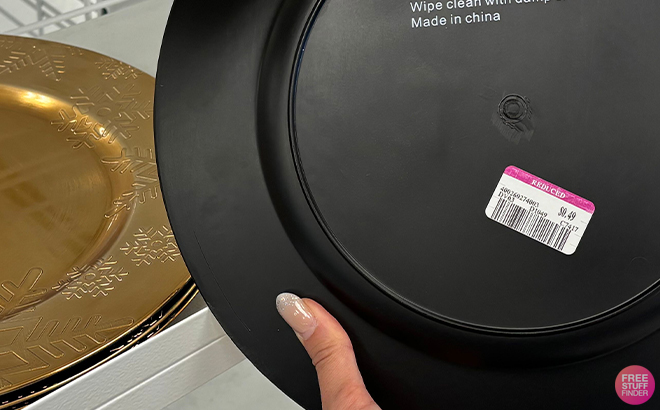 Hand Holding a Decorative Black Plate with a Gold Plate in The Background 49 Cent Ross Sale at Ross