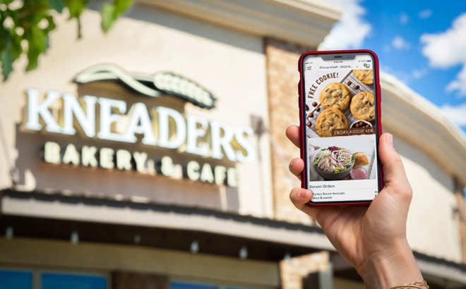 Hand Holding a Phone in Front of Kneaders Bakery Cafe Store